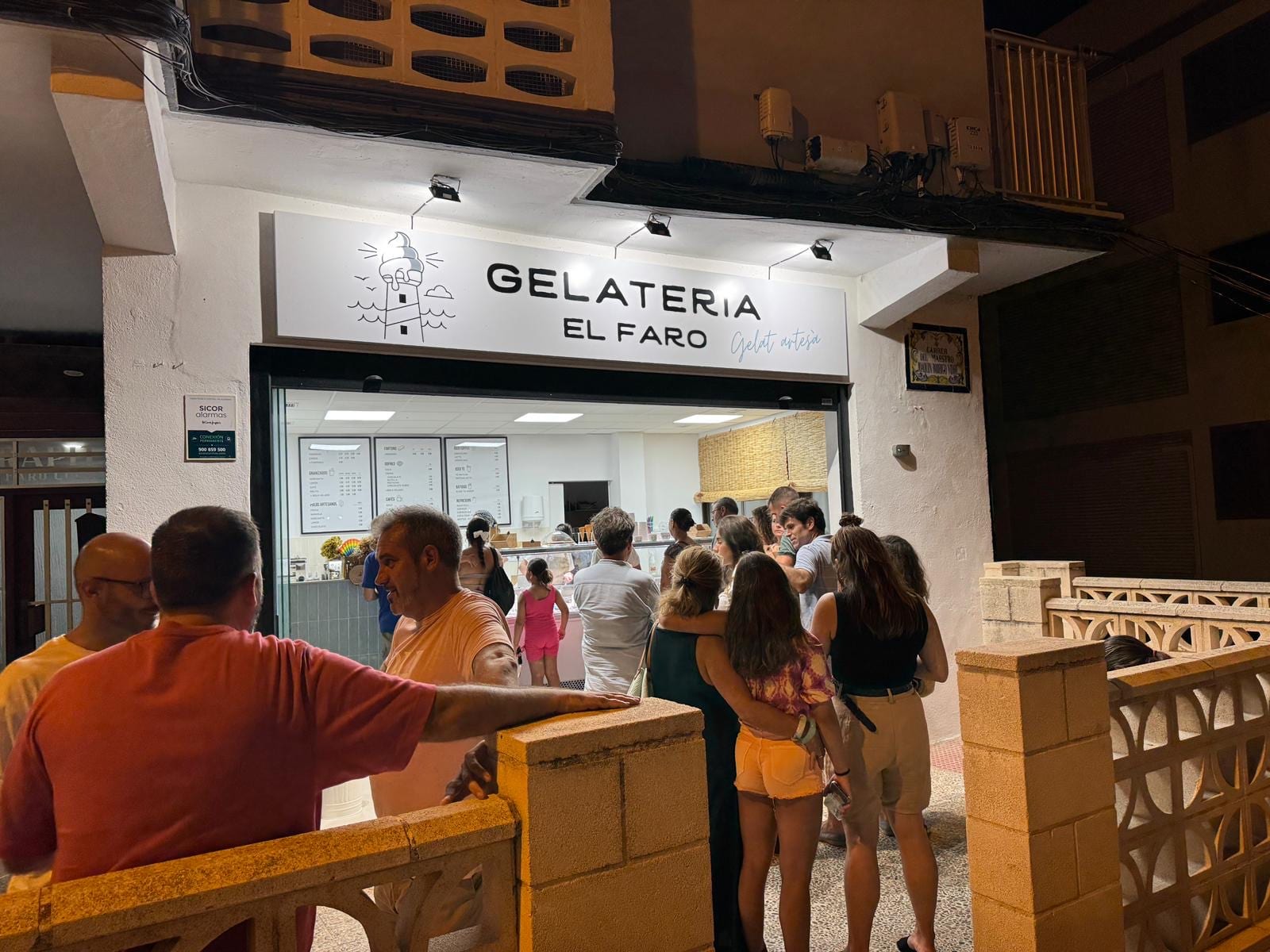 Customers queuing at Gelateria El Faro on a summer night, illuminated shop sign overhead