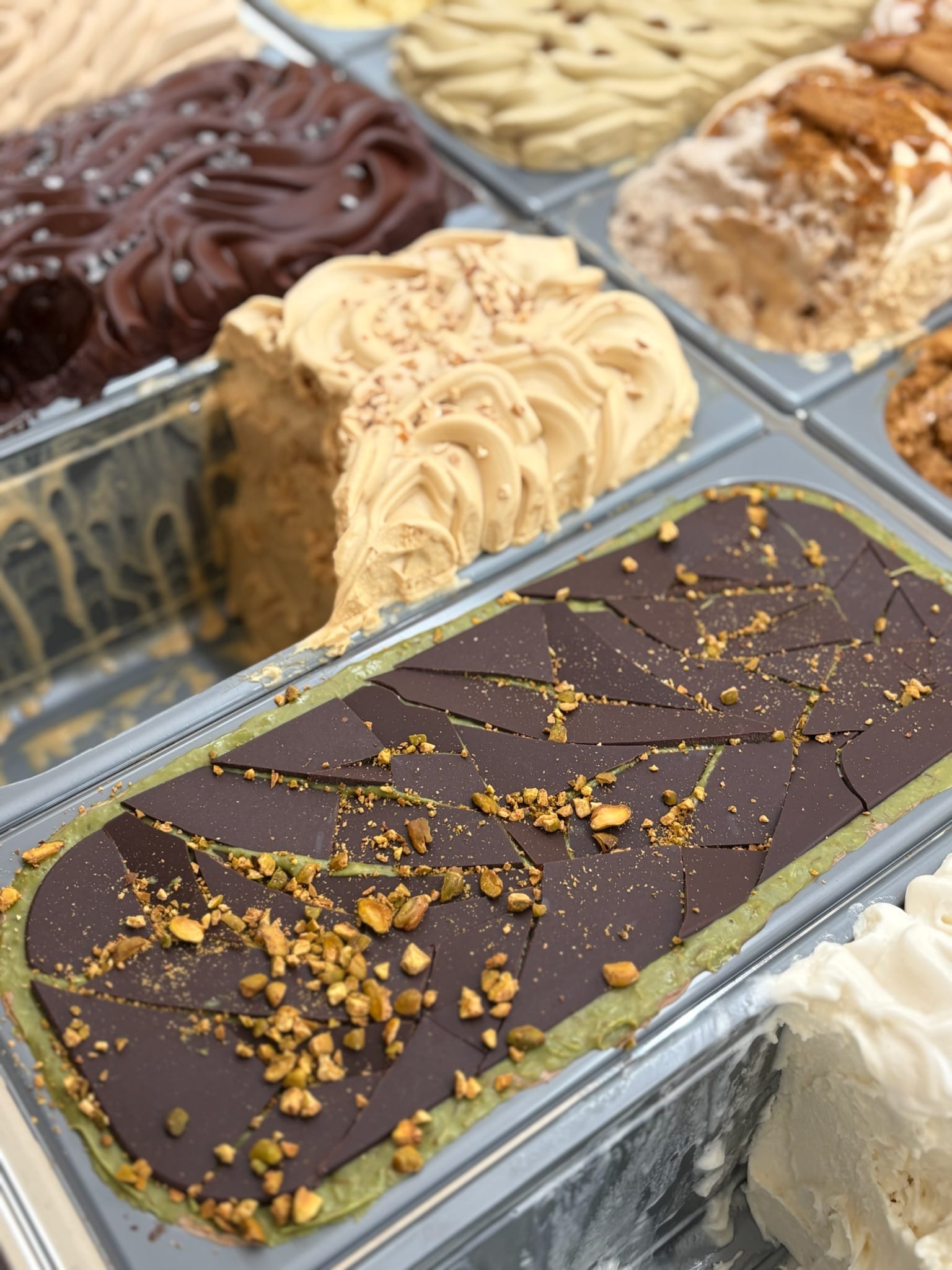 Pistachio ice cream tub topped with shattered dark-chocolate shards and crushed pistachio