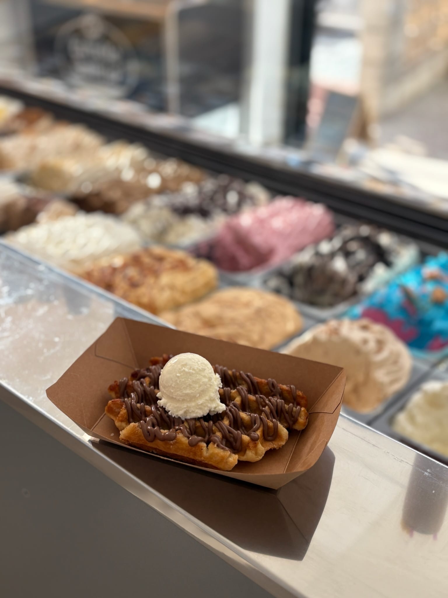 Freshly made waffle drizzled with chocolate and topped with a vanilla scoop